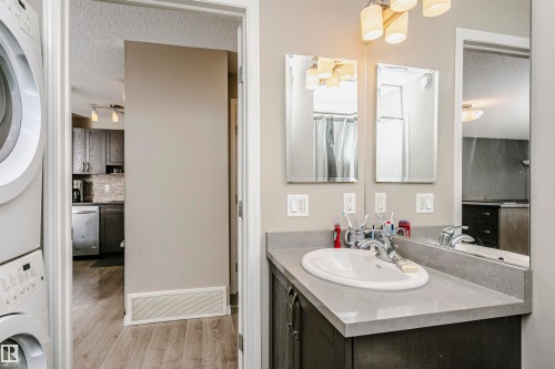 Bathroom with a textured ceiling, stacked washer / drying machine, vanity, light wood-style flooring, and backsplash - 4011 Orchards Drive, Edmonton, AB - Indoor Photo Showing Bathroom