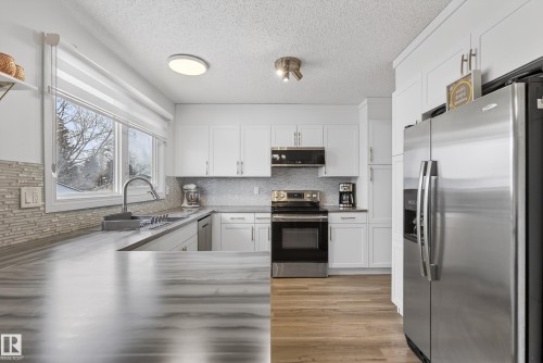 Kitchen featuring stainless steel appliances, white cabinetry, backsplash, a textured ceiling, and light wood-type flooring - 17303 101 Street, Edmonton, AB - Indoor Photo Showing Kitchen With Stainless Steel Kitchen With Upgraded Kitchen