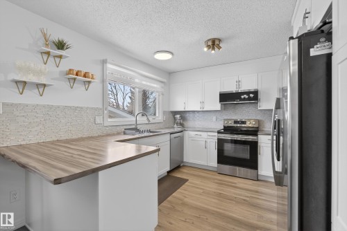 Kitchen with open shelves, stainless steel appliances, a peninsula, white cabinetry, and light wood-type flooring - 17303 101 Street, Edmonton, AB - Indoor Photo Showing Kitchen With Stainless Steel Kitchen