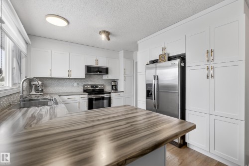 Kitchen with a peninsula, stainless steel appliances, white cabinets, backsplash, and a textured ceiling - 17303 101 Street, Edmonton, AB - Indoor Photo Showing Kitchen With Stainless Steel Kitchen With Upgraded Kitchen