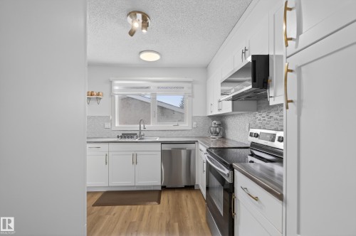 Kitchen featuring stainless steel appliances, white cabinets, light wood-type flooring, decorative backsplash, and a textured ceiling - 17303 101 Street, Edmonton, AB - Indoor Photo Showing Kitchen With Stainless Steel Kitchen