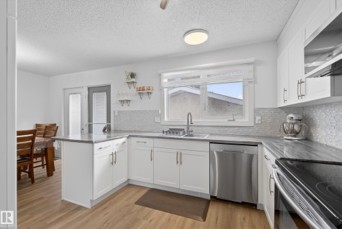 Kitchen featuring a peninsula, stainless steel appliances, white cabinets, backsplash, and a textured ceiling - 17303 101 Street, Edmonton, AB - Indoor Photo Showing Kitchen With Stainless Steel Kitchen