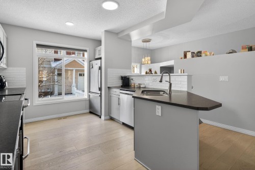 Kitchen featuring a peninsula, tasteful backsplash, stainless steel appliances, light wood-type flooring, and a textured ceiling - 60 1804 70 Street, Edmonton, AB - Indoor Photo Showing Kitchen With Double Sink With Upgraded Kitchen