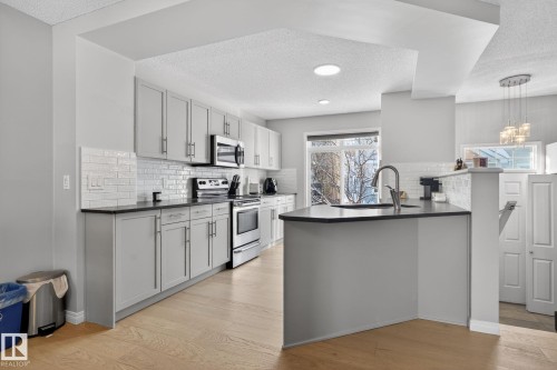 Kitchen featuring a textured ceiling, stainless steel appliances, a peninsula, light wood finished floors, and decorative backsplash - 60 1804 70 Street, Edmonton, AB - Indoor Photo Showing Kitchen With Upgraded Kitchen