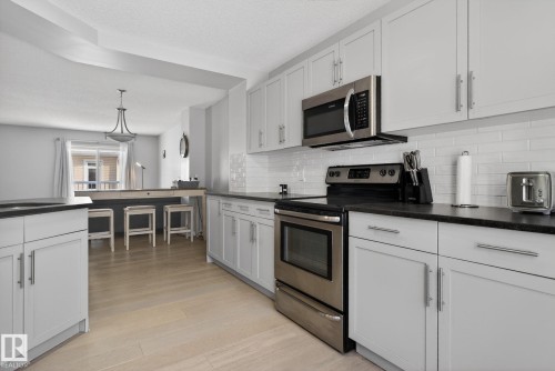Kitchen with electric stove, white cabinets, pendant lighting, light wood-style flooring, and backsplash - 60 1804 70 Street, Edmonton, AB - Indoor Photo Showing Kitchen With Upgraded Kitchen