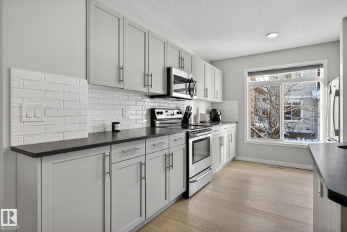 Kitchen with stainless steel appliances, dark countertops, light wood finished floors, a textured ceiling, and backsplash - 60 1804 70 Street, Edmonton, AB - Indoor Photo Showing Kitchen With Upgraded Kitchen