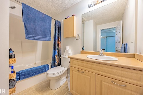 Bathroom with vanity, a textured ceiling, shower / bathtub combination with curtain, and light tile patterned floors - 132 6220 134 Avenue, Edmonton, AB - Indoor Photo Showing Bathroom