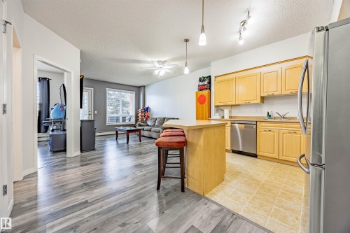 Kitchen featuring light wood finish cabinetry, stainless steel appliances, light countertops, a textured ceiling, and open floor plan - 132 6220 134 Avenue, Edmonton, AB - Indoor Photo Showing Kitchen