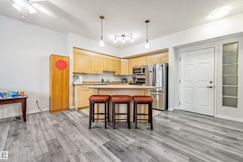 Kitchen with light countertops, light wood finish cabinets, a kitchen island, a breakfast bar area, and stainless steel appliances - 132 6220 134 Avenue, Edmonton, AB - Indoor Photo Showing Kitchen