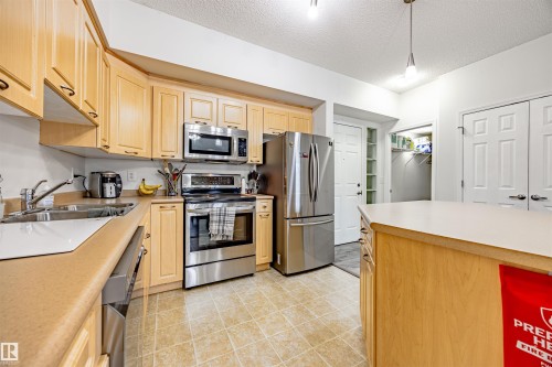 Kitchen featuring stainless steel appliances, light wood finish cabinets, light countertops, a textured ceiling, and decorative light fixtures - 132 6220 134 Avenue, Edmonton, AB - Indoor Photo Showing Kitchen With Stainless Steel Kitchen With Double Sink