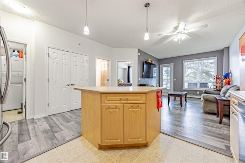 Kitchen with a textured ceiling, ceiling fan, a kitchen island, open floor plan, and stacked washing machine and dryer - 132 6220 134 Avenue, Edmonton, AB - Indoor Photo Showing Other Room