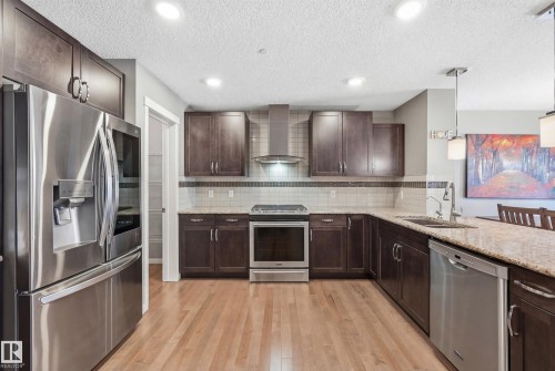 Kitchen with stainless steel appliances, dark wood finish cabinets, light stone countertops, light wood finished floors, and a textured ceiling - 2031 Westerra Loop, Stony Plain, AB - Indoor Photo Showing Kitchen With Upgraded Kitchen
