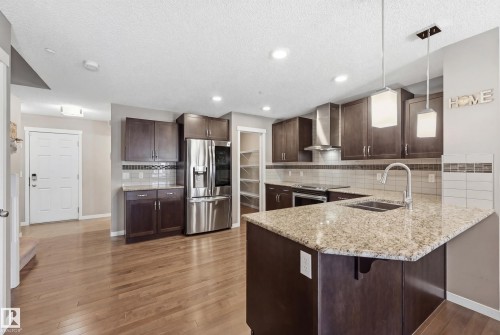 Kitchen with dark wood finish cabinets, a peninsula, pendant lighting, stainless steel appliances, and light stone counters - 2031 Westerra Loop, Stony Plain, AB - Indoor Photo Showing Kitchen With Double Sink With Upgraded Kitchen