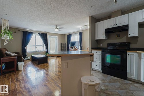 Kitchen with black range with electric stovetop, open floor plan, healthy amount of natural light, white cabinets, and a textured ceiling - 314 5340 199 Street, Edmonton, AB - Indoor Photo Showing Kitchen