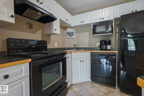 Kitchen with black appliances, white cabinets, dark countertops, a textured ceiling, and light tile patterned floors - 314 5340 199 Street, Edmonton, AB - Indoor Photo Showing Kitchen