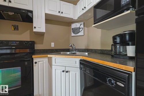 Kitchen featuring black appliances, dark countertops, white cabinetry, and range hood - 314 5340 199 Street, Edmonton, AB - Indoor Photo Showing Kitchen With Double Sink
