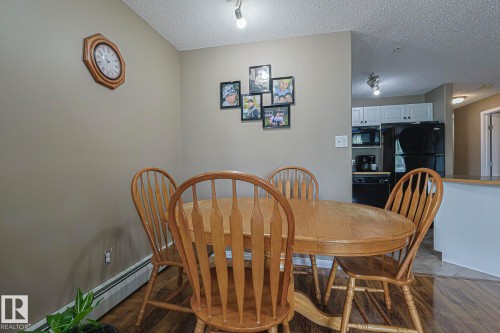 Dining area with a textured ceiling, a baseboard heating unit, and dark wood-style floors - 314 5340 199 Street, Edmonton, AB - Indoor Photo Showing Dining Room