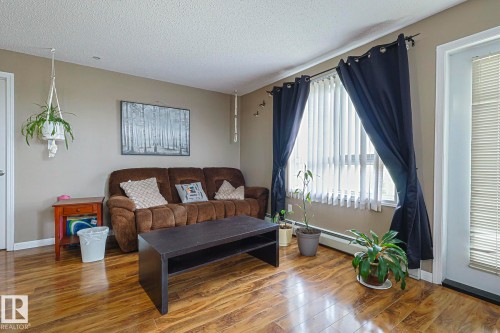 Living area featuring wood finished floors, baseboard heating, and a textured ceiling - 314 5340 199 Street, Edmonton, AB - Indoor Photo Showing Living Room