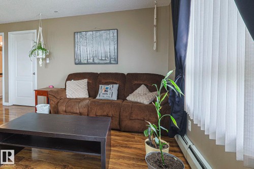 Living room with a baseboard heating unit, wood finished floors, and a textured ceiling - 314 5340 199 Street, Edmonton, AB - Indoor Photo Showing Living Room