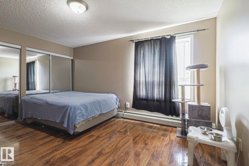 Bedroom featuring a textured ceiling, baseboard heating, dark wood-type flooring, and two closets - 314 5340 199 Street, Edmonton, AB - Indoor Photo Showing Bedroom