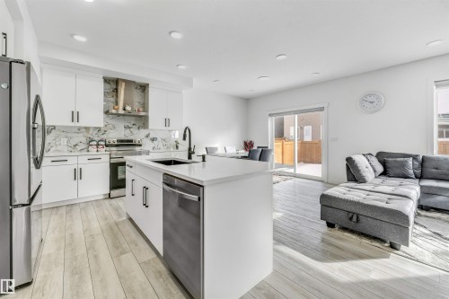 Kitchen featuring white cabinetry, a center island with sink, stainless steel appliances, open floor plan, and light wood-style flooring - 2629 15A Avenue, Edmonton, AB - Indoor