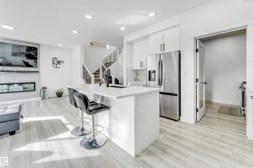 Kitchen with white cabinetry, stainless steel fridge, an island with sink, light wood-style floors, and a kitchen bar - 2629 15A Avenue, Edmonton, AB - Indoor Photo Showing Kitchen With Upgraded Kitchen