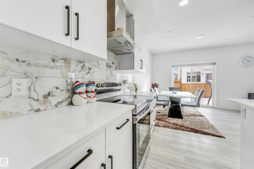 Kitchen with white cabinetry, stainless steel electric range oven, tasteful backsplash, light wood-style flooring, and light stone countertops - 2629 15A Avenue, Edmonton, AB - Indoor Photo Showing Kitchen