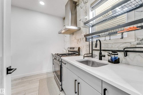 Kitchen featuring gas range, light wood-style floors, light stone countertops, and decorative backsplash - 2629 15A Avenue, Edmonton, AB - Indoor Photo Showing Kitchen