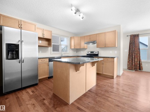 Kitchen with a kitchen bar, stainless steel appliances, a textured ceiling, dark wood-style floors, and light wood finish cabinets - 1708 62 Street, Edmonton, AB - Indoor Photo Showing Kitchen
