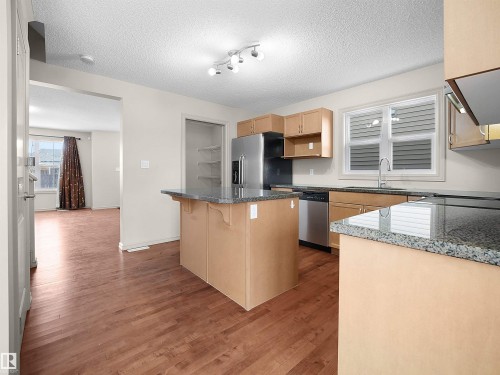 Kitchen featuring a kitchen bar, light wood finish cabinets, a center island, dark wood-style flooring, and a textured ceiling - 1708 62 Street, Edmonton, AB - Indoor Photo Showing Kitchen