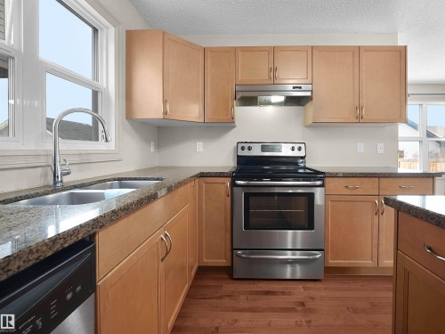 Kitchen featuring stainless steel appliances, dark stone countertops, a textured ceiling, and dark wood-style flooring - 1708 62 Street, Edmonton, AB - Indoor Photo Showing Kitchen With Double Sink