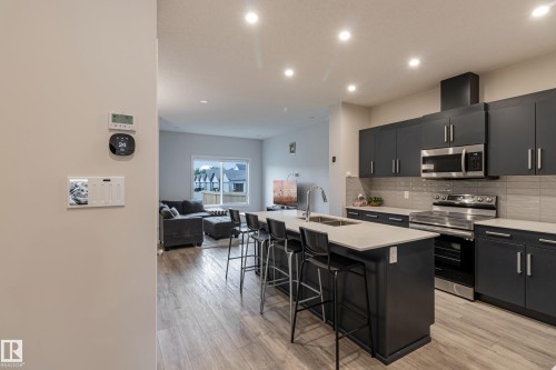 Kitchen featuring stainless steel appliances, a kitchen island with sink, dark cabinetry, a kitchen bar, and open floor plan - 304 36 Avenue, Edmonton, AB - Indoor Photo Showing Kitchen With Upgraded Kitchen