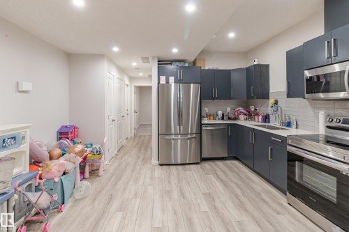Kitchen featuring stainless steel appliances, light wood-style floors, recessed lighting, tasteful backsplash, and light stone countertops - 304 36 Avenue, Edmonton, AB - Indoor Photo Showing Kitchen With Double Sink
