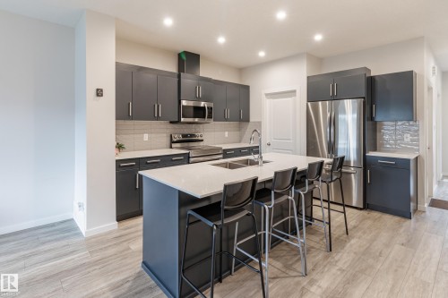 Kitchen with stainless steel appliances, a kitchen island with sink, light stone counters, light wood finished floors, and a breakfast bar - 304 36 Avenue, Edmonton, AB - Indoor Photo Showing Kitchen With Double Sink With Upgraded Kitchen