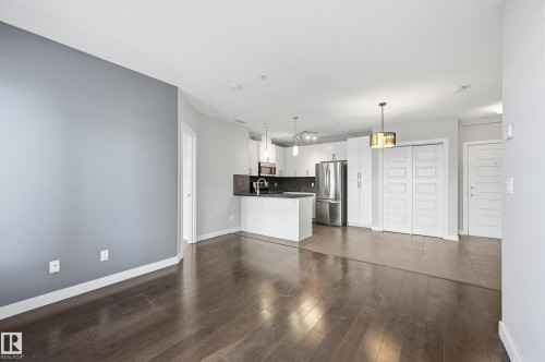 Unfurnished living room with dark wood finished floors and baseboards - 511 5151 Windermere Boulevard, Edmonton, AB - Indoor Photo Showing Kitchen