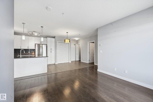 Unfurnished living room featuring dark wood-type flooring and baseboards - 511 5151 Windermere Boulevard, Edmonton, AB - Indoor Photo Showing Kitchen