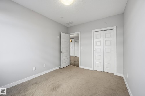 Unfurnished bedroom with light colored carpet, a closet, and a textured ceiling - 511 5151 Windermere Boulevard, Edmonton, AB - Indoor Photo Showing Other Room