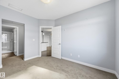 Unfurnished bedroom with light colored carpet and ensuite bath - 511 5151 Windermere Boulevard, Edmonton, AB - Indoor Photo Showing Other Room
