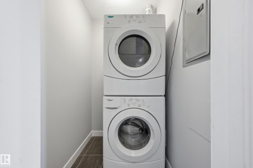Laundry area featuring electric panel and stacked washer and clothes dryer - 511 5151 Windermere Boulevard, Edmonton, AB - Indoor Photo Showing Laundry Room