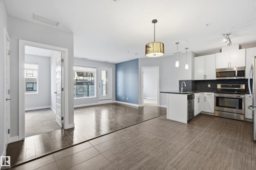 Kitchen with stainless steel appliances, backsplash, white cabinetry, decorative light fixtures, and open floor plan - 511 5151 Windermere Boulevard, Edmonton, AB - Indoor Photo Showing Kitchen