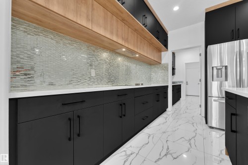 Dual tone kitchen with dual tone cabinets, stainless steel fridge, light marble finish floors, recessed lighting, and tasteful backsplash - 16812 48 Street Nw, Edmonton, AB - Indoor Photo Showing Kitchen