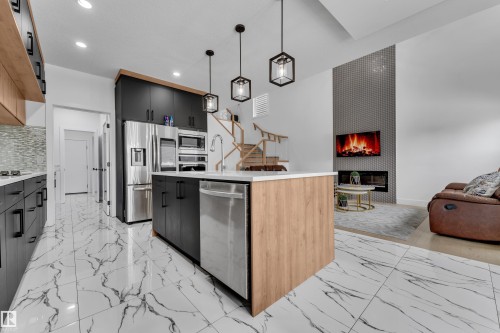 Kitchen featuring a kitchen island with sink, modern cabinets, a fireplace, stainless steel appliances, and light marble finish flooring - 16812 48 Street Nw, Edmonton, AB - Indoor Photo Showing Kitchen With Upgraded Kitchen