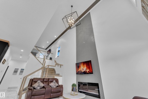Living area featuring a high ceiling, a large fireplace, suspended lighting, and marble finish floors - 16812 48 Street Nw, Edmonton, AB - Indoor With Fireplace