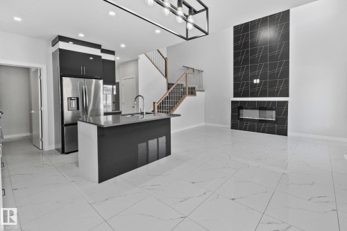 Kitchen with a center island with sink, stainless steel fridge with ice dispenser, modern cabinets, dark cabinetry, and a fireplace - 3524 41 Ave, Beaumont, AB - Indoor