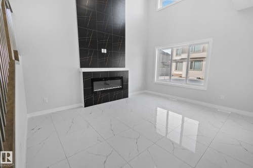 Unfurnished living room featuring a high ceiling, light marble finish floors, and a tile fireplace - 3524 41 Ave, Beaumont, AB - Indoor Photo Showing Other Room With Fireplace