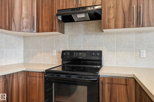 Kitchen featuring black range with electric stovetop, wood finish cabinetry, range hood, decorative backsplash, and light stone countertops - 1346 Cunningham Drive W, Edmonton, AB - Indoor Photo Showing Kitchen