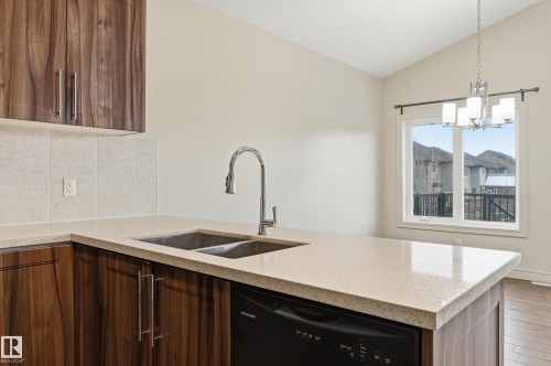 Kitchen featuring light stone counters, dishwasher, lofted ceiling, a peninsula, and decorative backsplash - 1346 Cunningham Drive W, Edmonton, AB - Indoor Photo Showing Kitchen With Double Sink