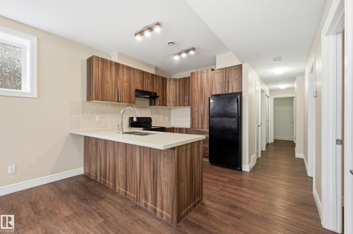 Kitchen with wood finish cabinets, black appliances, a peninsula, tasteful backsplash, and dark wood-style floors - 1346 Cunningham Drive W, Edmonton, AB - Indoor Photo Showing Kitchen