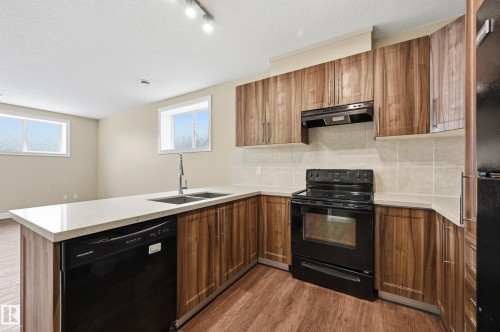 Kitchen with black appliances, wood finish cabinetry, tasteful backsplash, and a textured ceiling - 1346 Cunningham Drive W, Edmonton, AB - Indoor Photo Showing Kitchen With Double Sink
