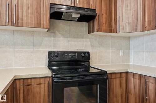 Kitchen featuring black / electric stove, wood finish cabinetry, light stone counters, and backsplash - 1346 Cunningham Drive W, Edmonton, AB - Indoor Photo Showing Kitchen